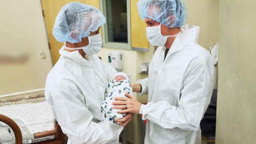 gay parents through surrogacy hold their newborn baby in the hospital