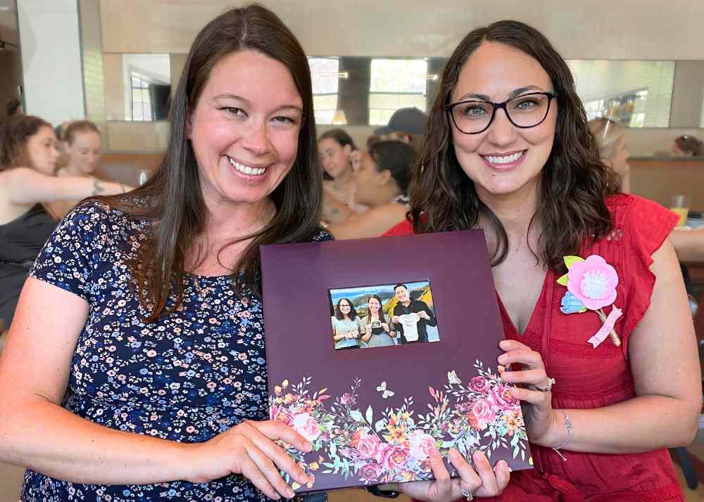 surrogate mother and intended mother holding surrogacy scrapbook